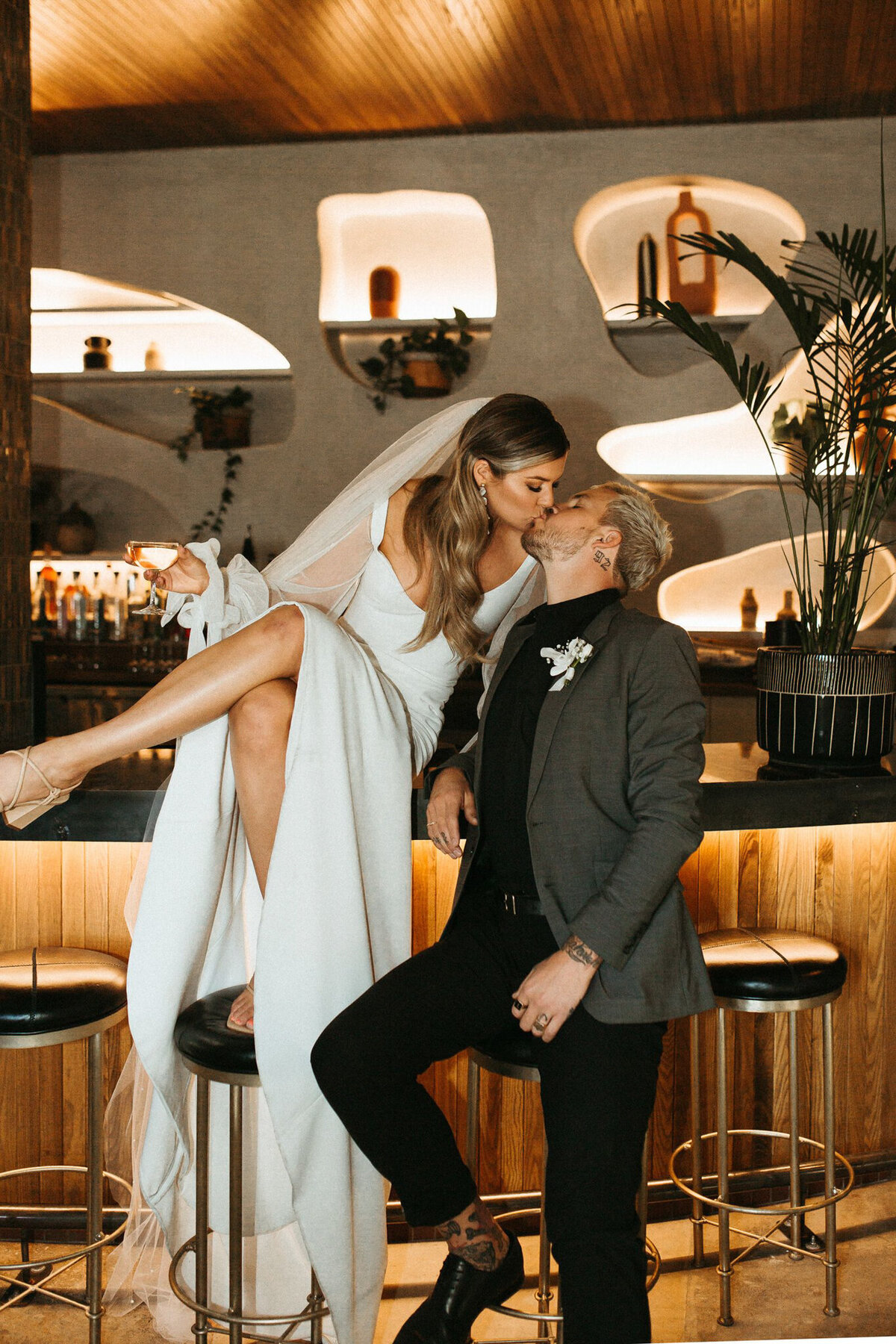 Bride and groom kissing on the bar at Fortuna’s Row, a historical wedding venue with an industrial vibe in Calgary. It has been featured on the Brontë Bride Vendor Guide.