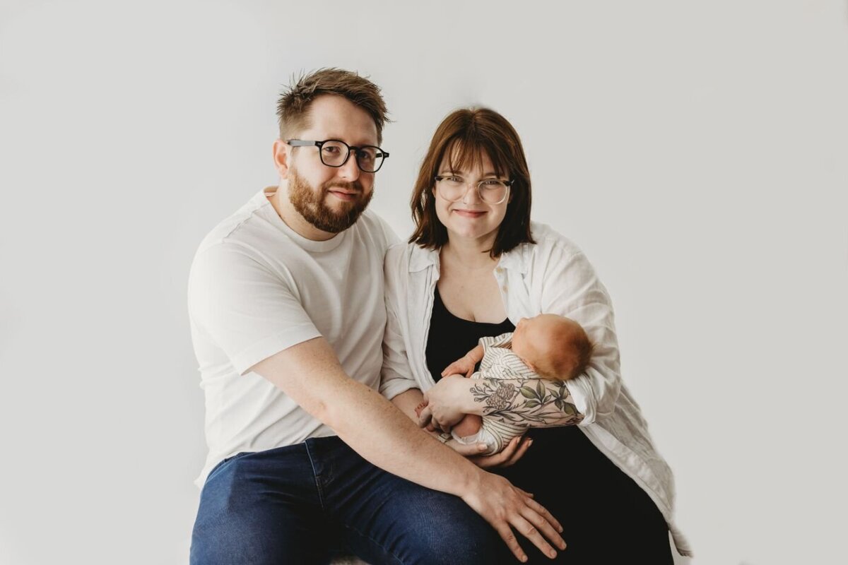 A heartwarming studio portrait of a proud mother and father sitting closely together while cradling their precious newborn baby. Newborn family photography