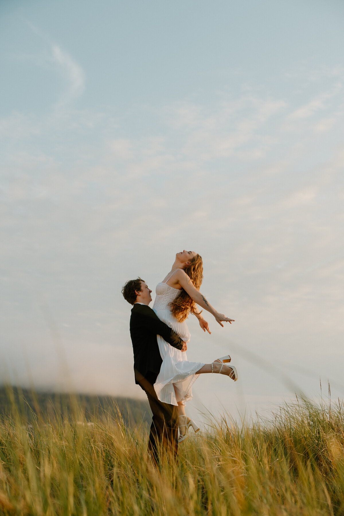 A man and woman spin in a field at sunset at Seaside, Oregon, during their engagement photos. 