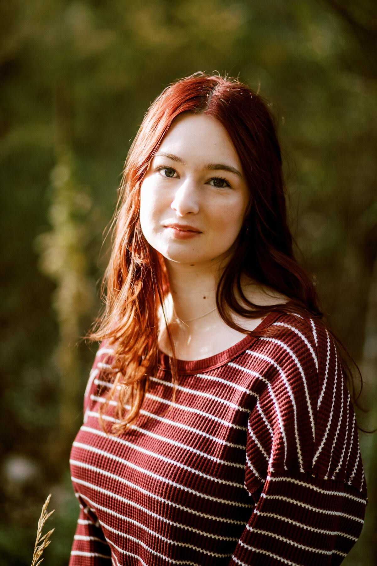High school senior girl with red hair sits in beautiful light