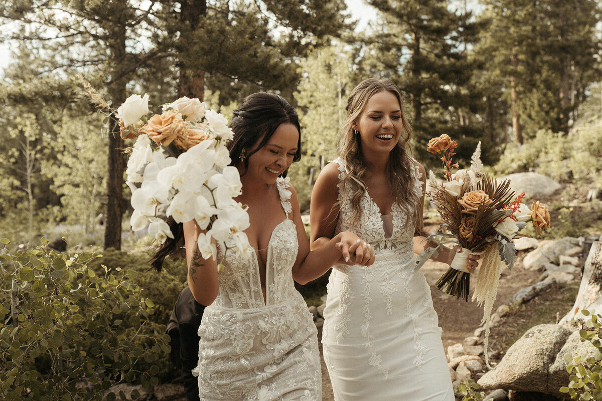 Two brides laughing with their wedding dresses and bouquets