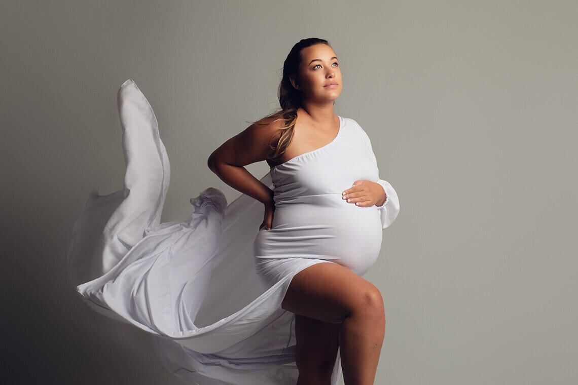 Pregnant woman holding bump wearing a white flowy dress