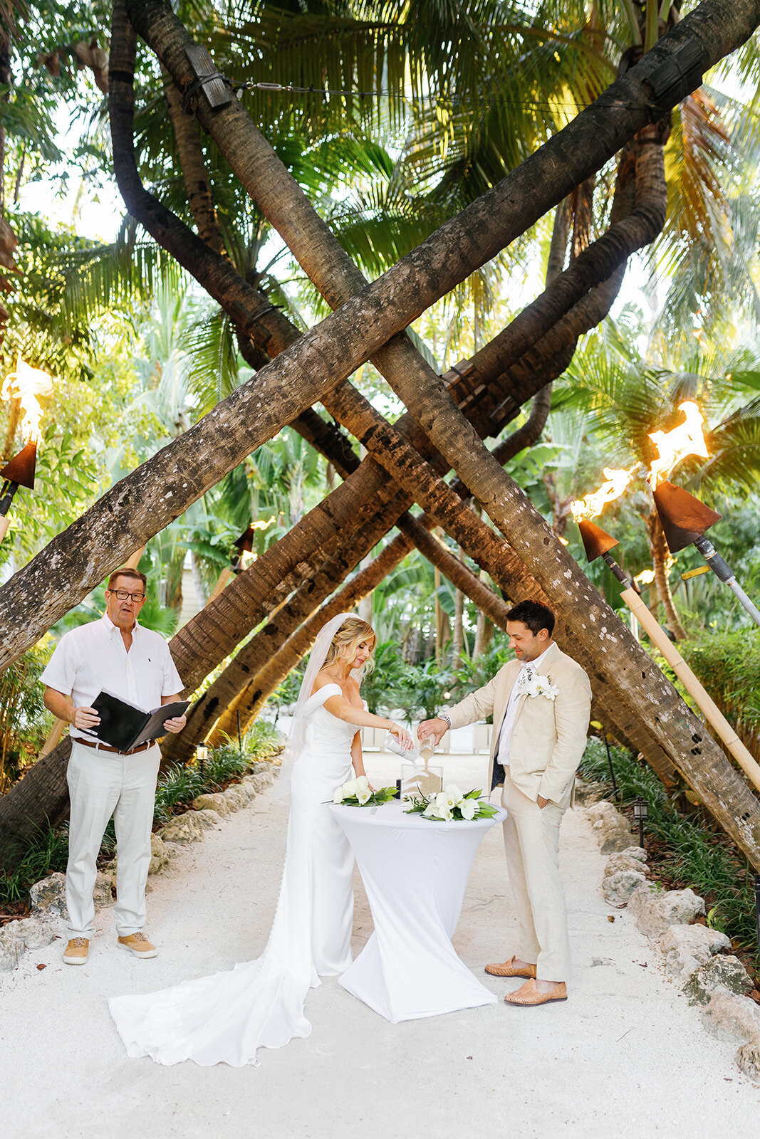 Monica and Austyn pour sand into a decorative glass container, symbolizing their unity in a beautiful Florida Keys wedding tradition.