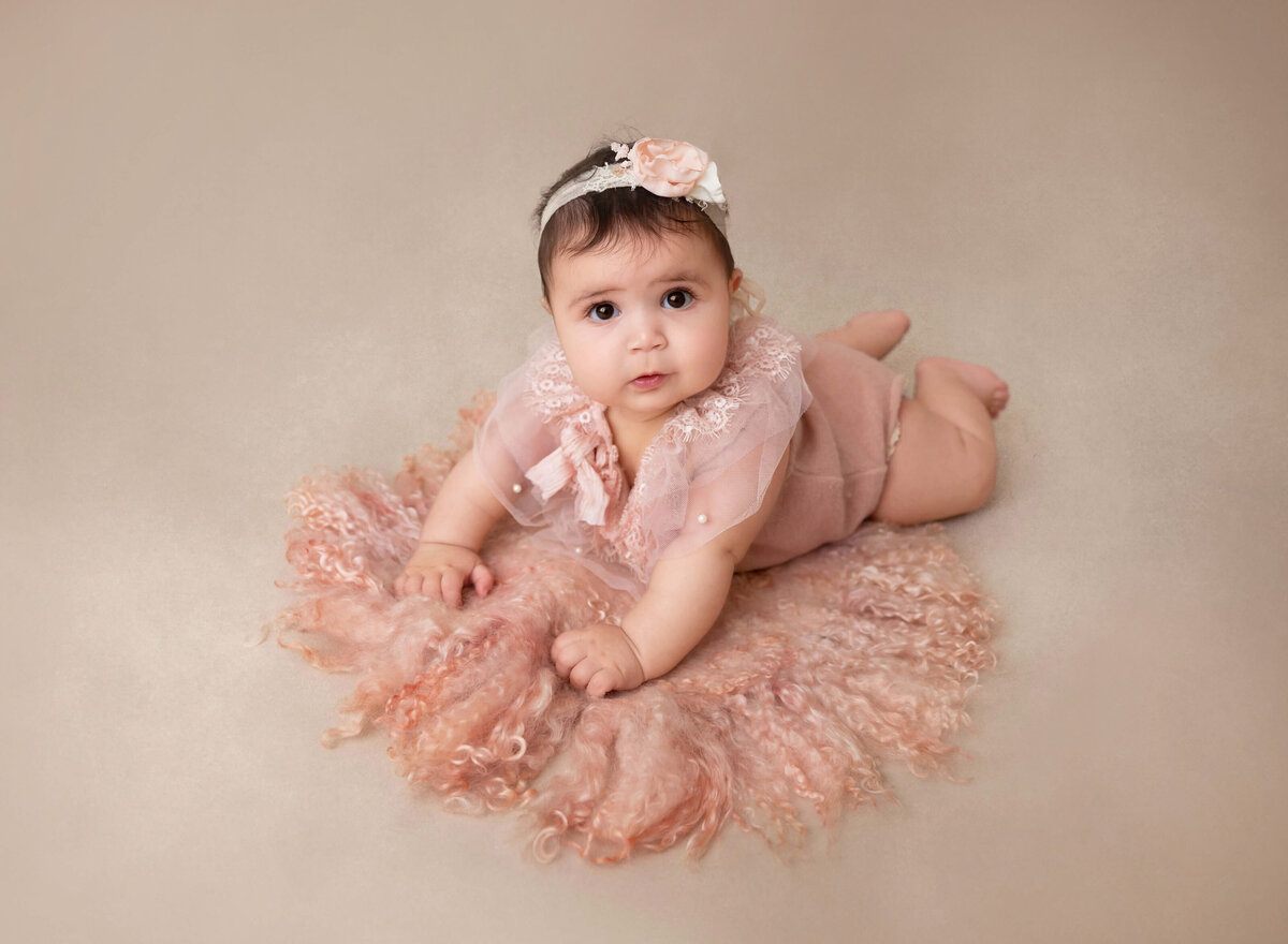 6-month baby girl is lying on her belly for a milestone photoshoot. Baby has her head lifted and is looking at the camera