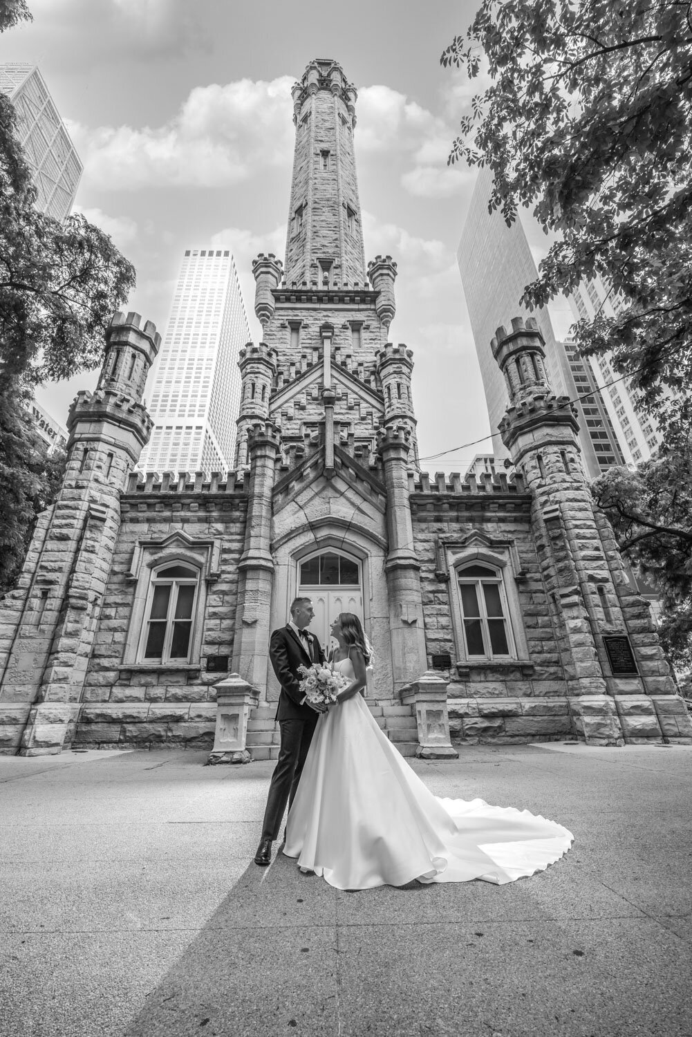 A black and white photo of a bride and groom in front of a castle