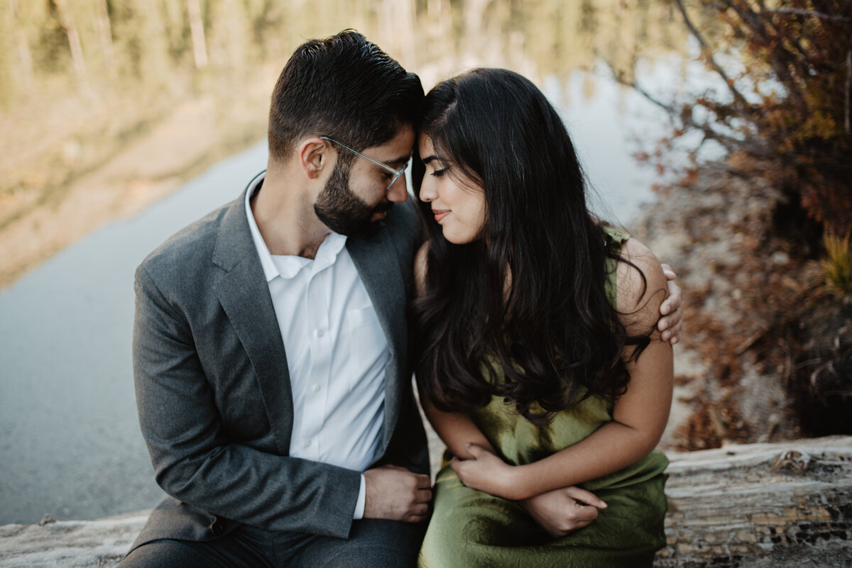 mand and woman with their foreheads together and their eyes closed as they sit on a log and embrace either other near a Jackson HOle lake for a fall engagement session