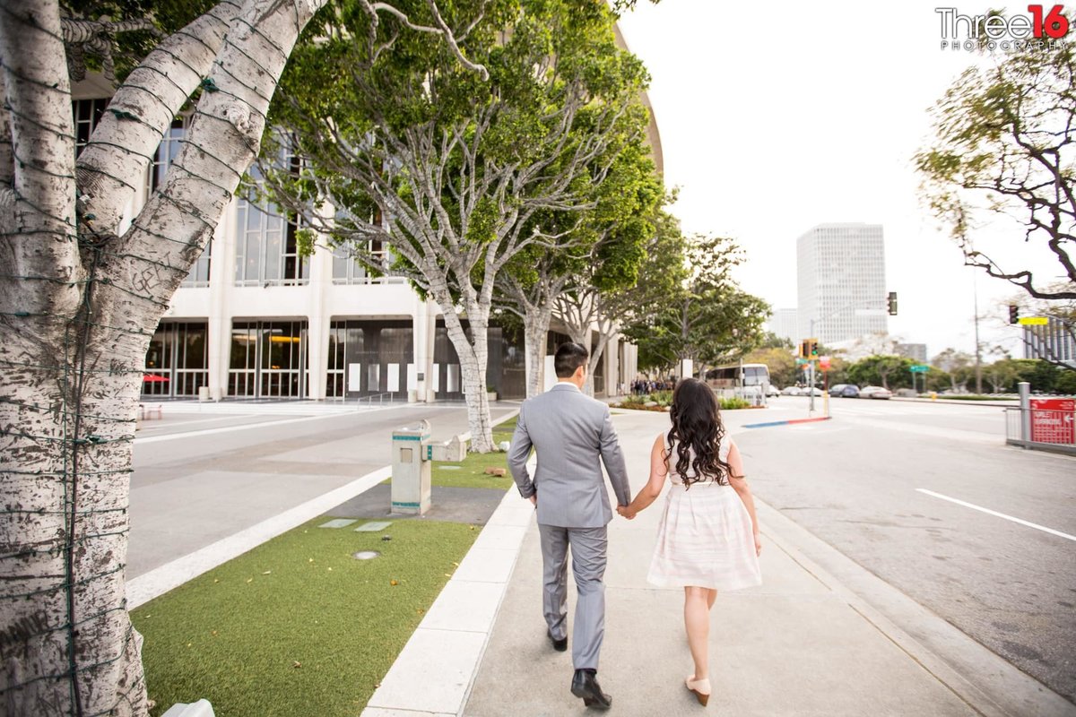 Engaged couple walk hand in hand down the street in downtown LA