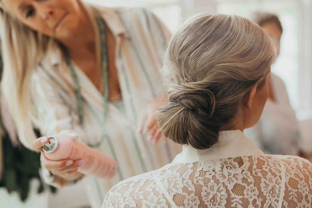 makeup artist sprays brides hair for her wedding day.