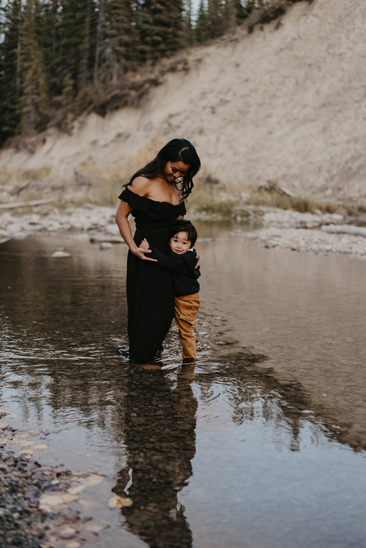 woman in black dress with her child stands in water