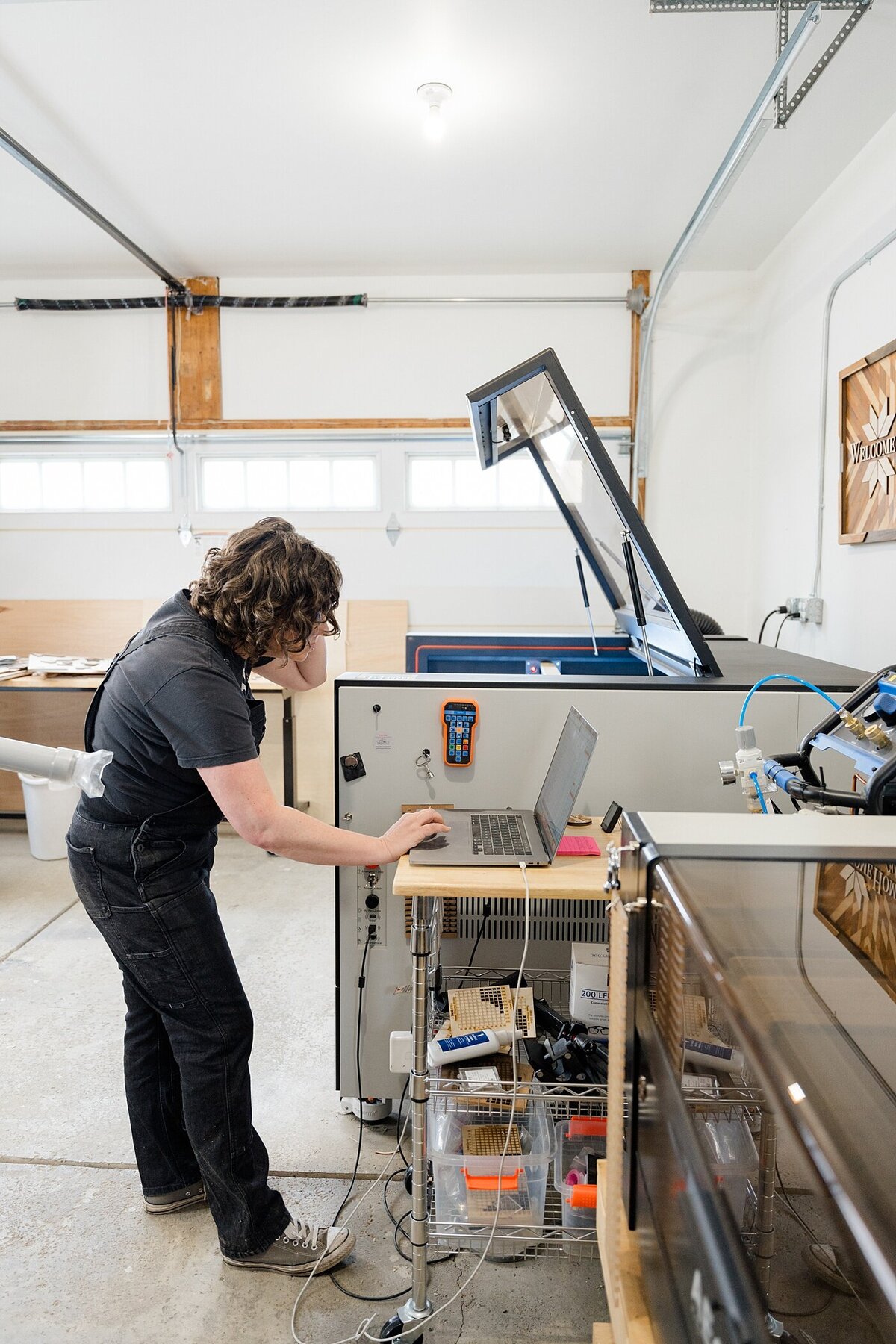behind the scenes branding photos with woman working on a computer that is hooked up to a large laser cutting machine