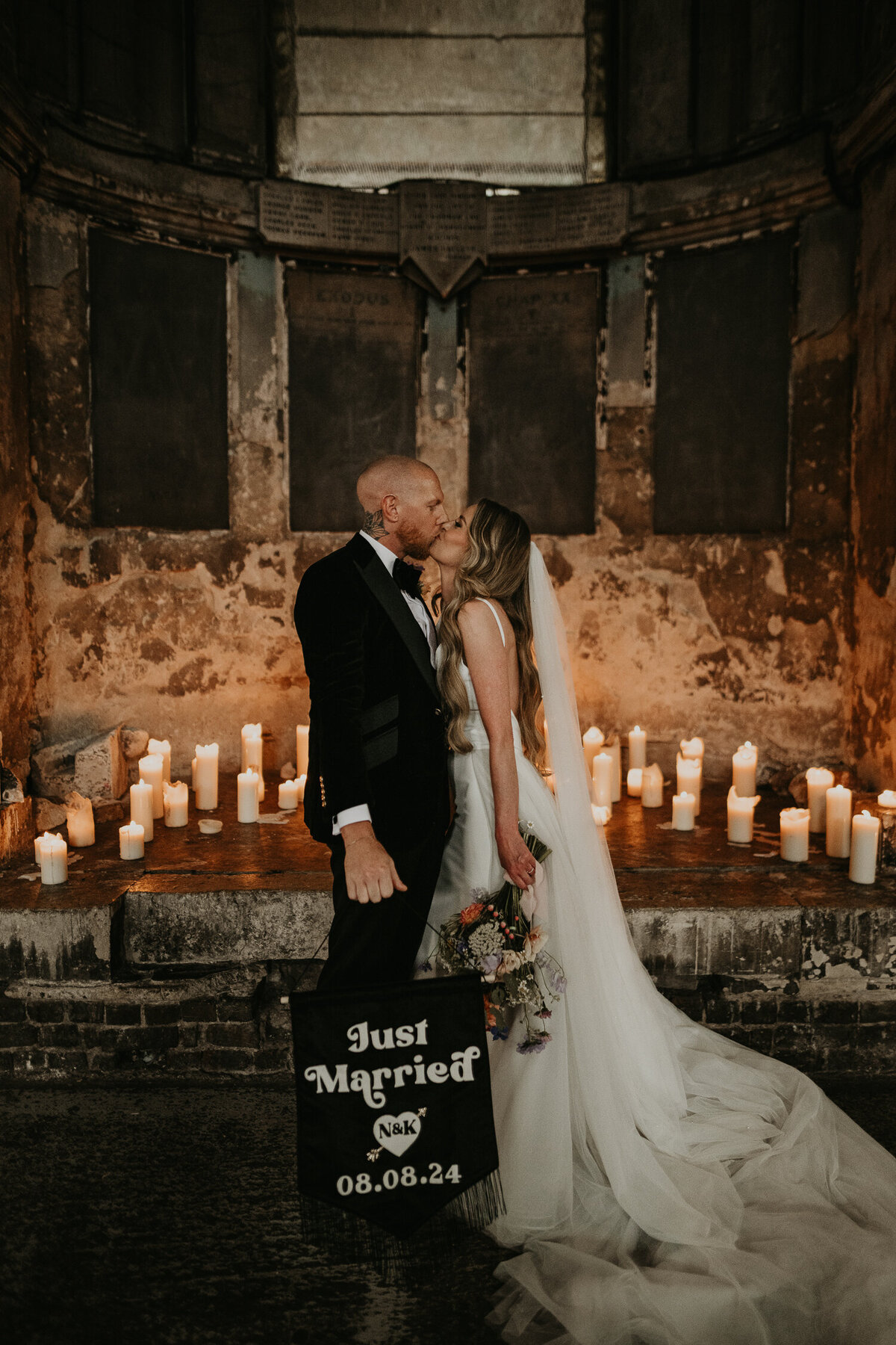 A bride and groom kiss in front of the candles at The Asylum Chapel.