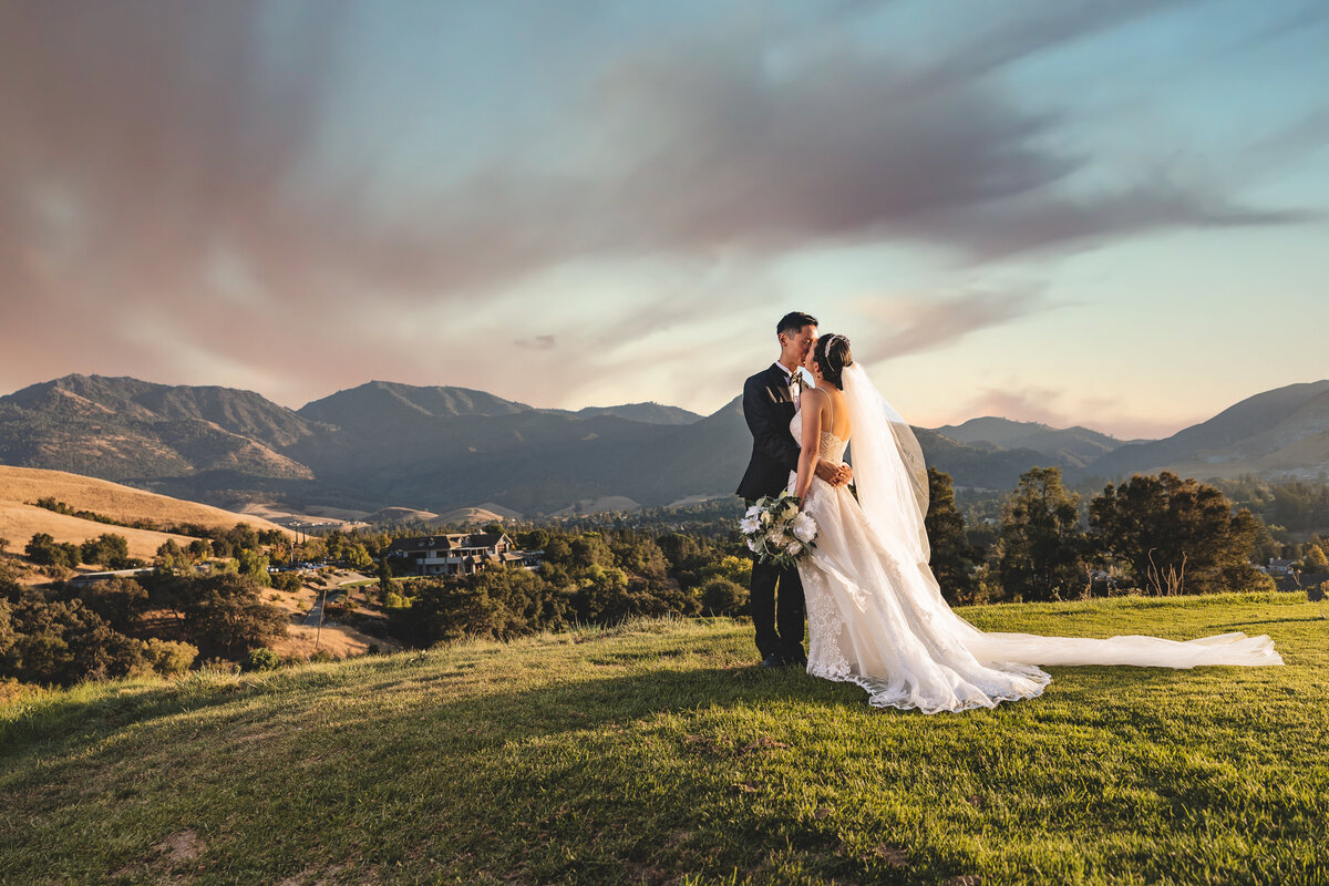 Bride and groom kiss on the top of a mountain with other mountains in the background and a dramatic sky. Photo captured by sacramento wedding photographer, philippe studio pro.