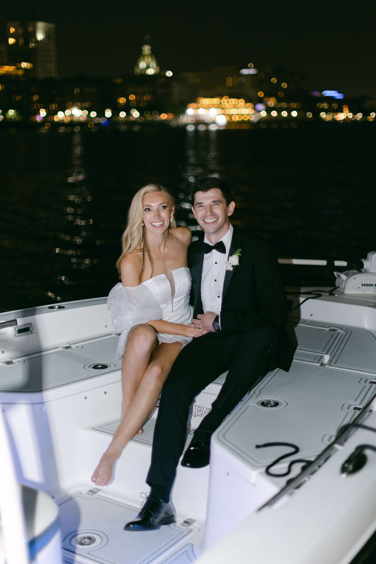 A bride and groom smile while sitting on the aft of a boat.