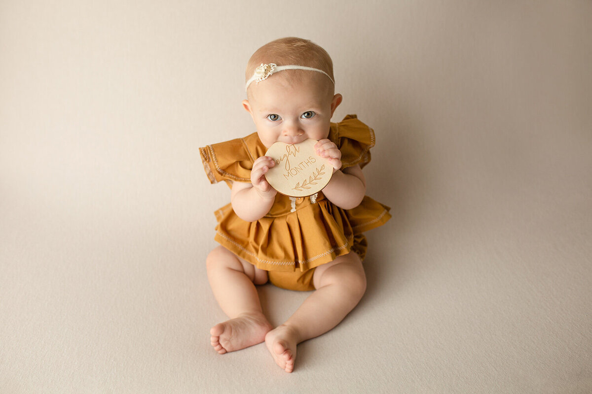 baby girl in yellow dress biting name card looking at the camera
