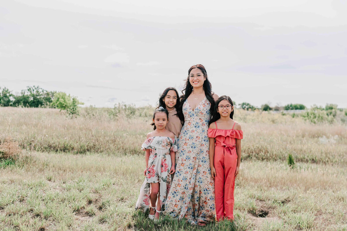 Mom and her 3 girls stand in a grassy field . 