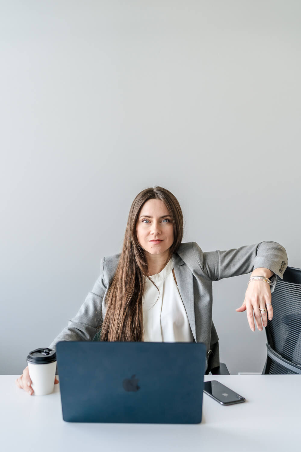 Confident coach on laptop holding takeout coffee in one hand and the other on the back of a chair for modern branding photos