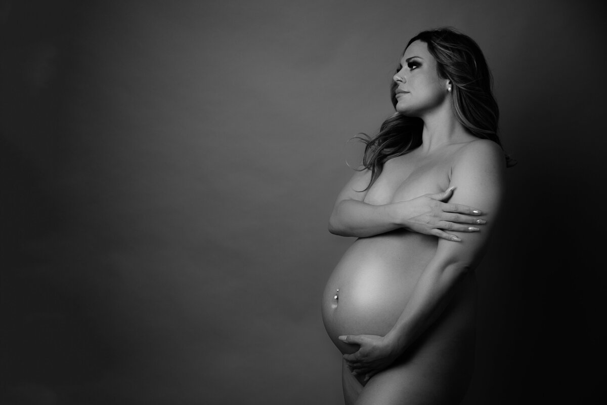 A portrait of a pregnant woman  naked covering her boobs with one hand and with the other touching her baby bump