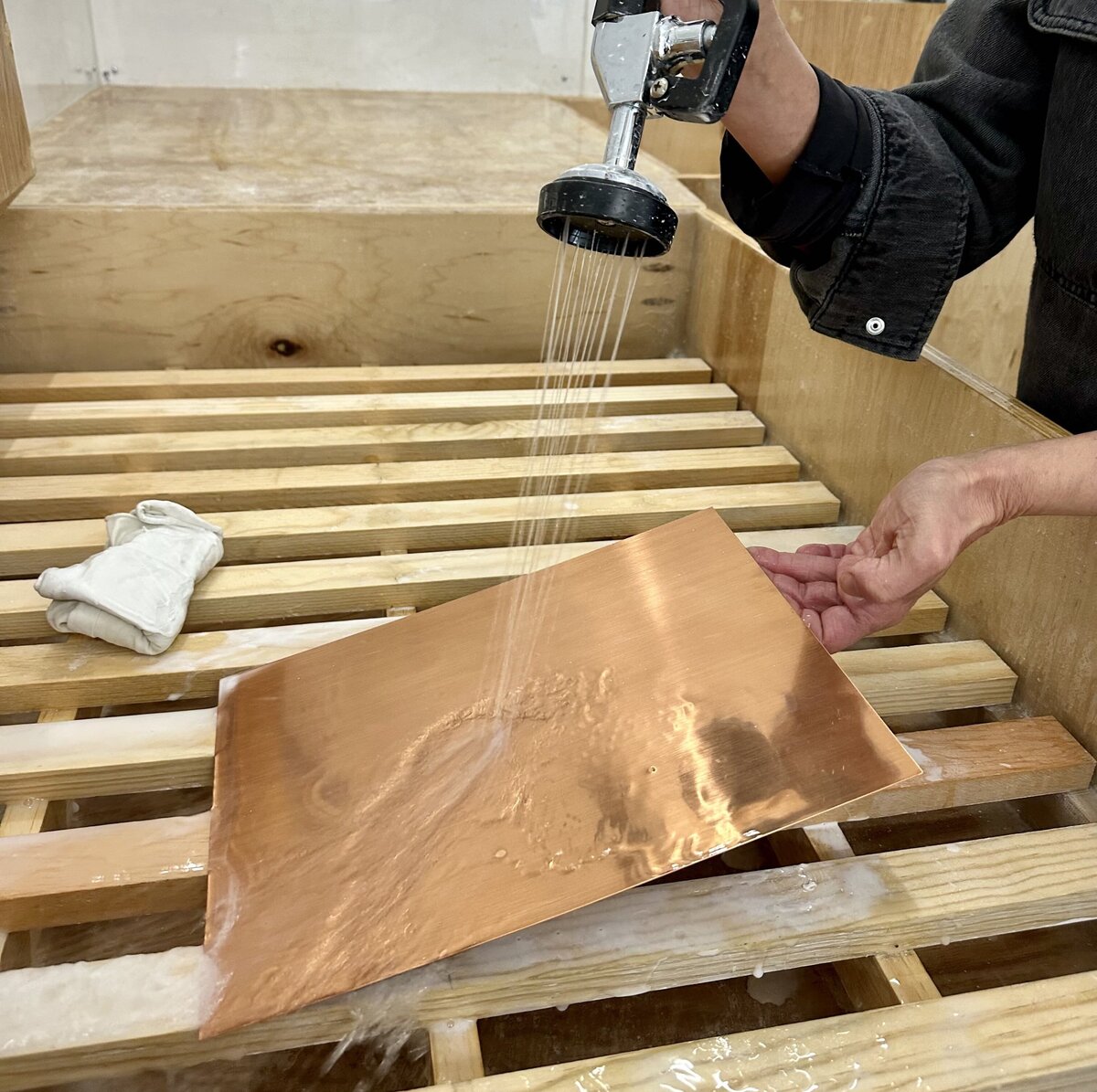 A printmaker rinsing a copper plate with water after etching, in preparation for printing in a printmaking studio.