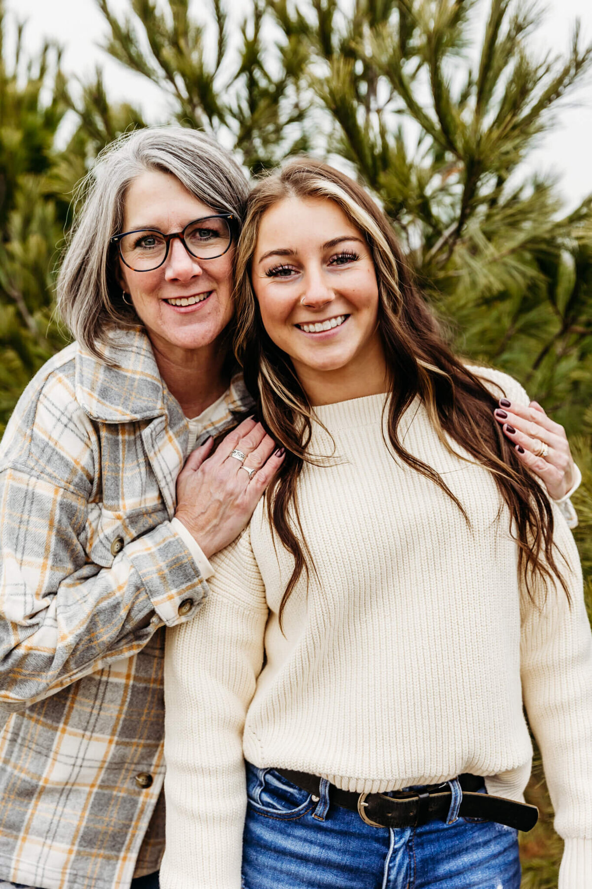 Mom in plaid hugging her daughter in white sweater during their family photo session with Ashley Kalbus