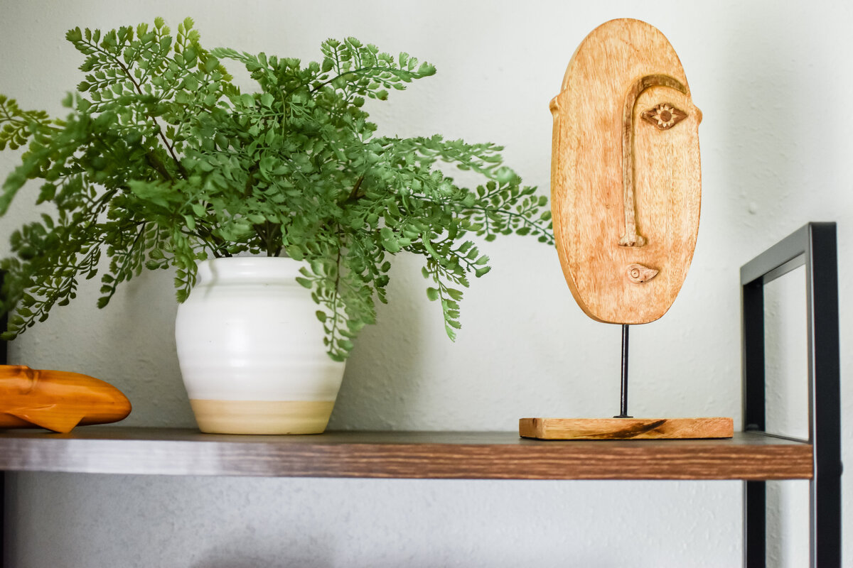 A modern stature of an abstract face sits on the top of a bookshelf next to a plant