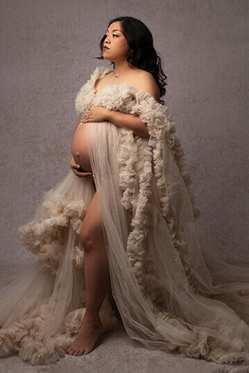 A mom to be in a tan tule maternity gown stoically holds her bumpNew Orleans Maternity Photographer