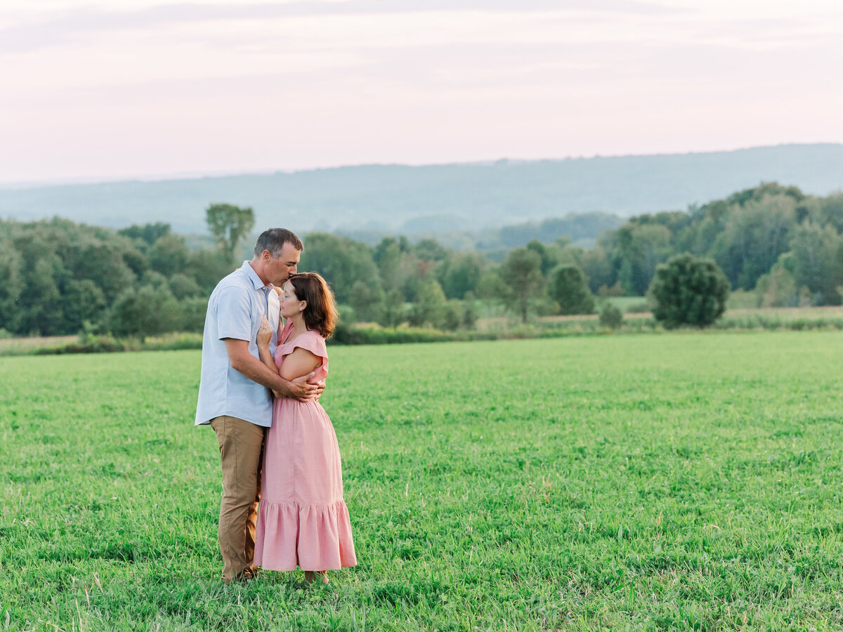 Husband and wife hugging in a field outdoors at sunset for couple’s photography.