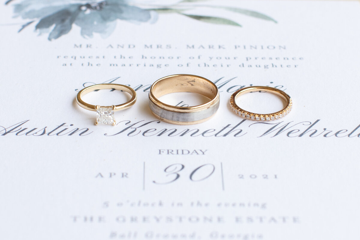 3 gold wedding bands lined up on invitation detail by Firefly Photography