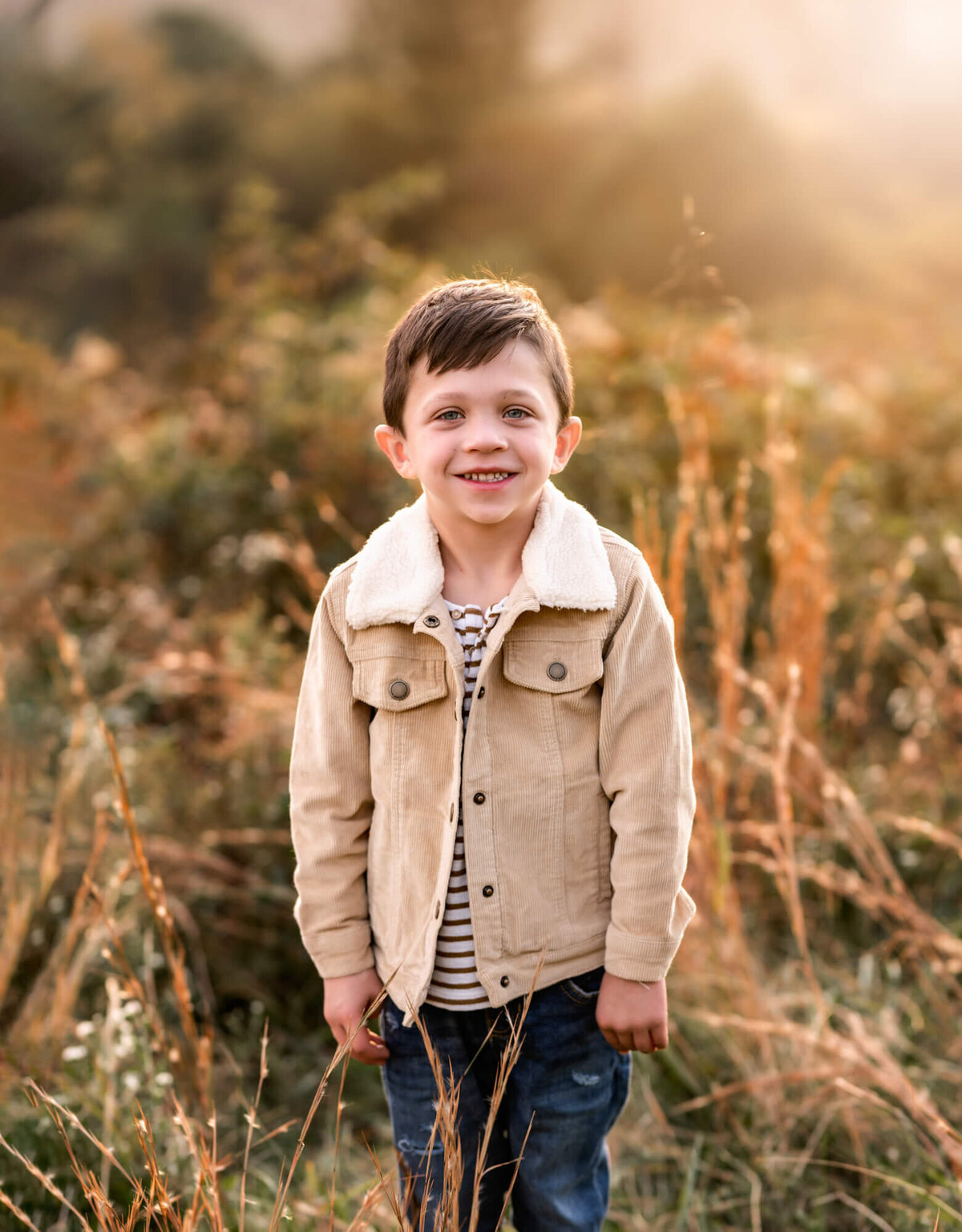 A cute little boy in a corduroy jacket standing the tall grass