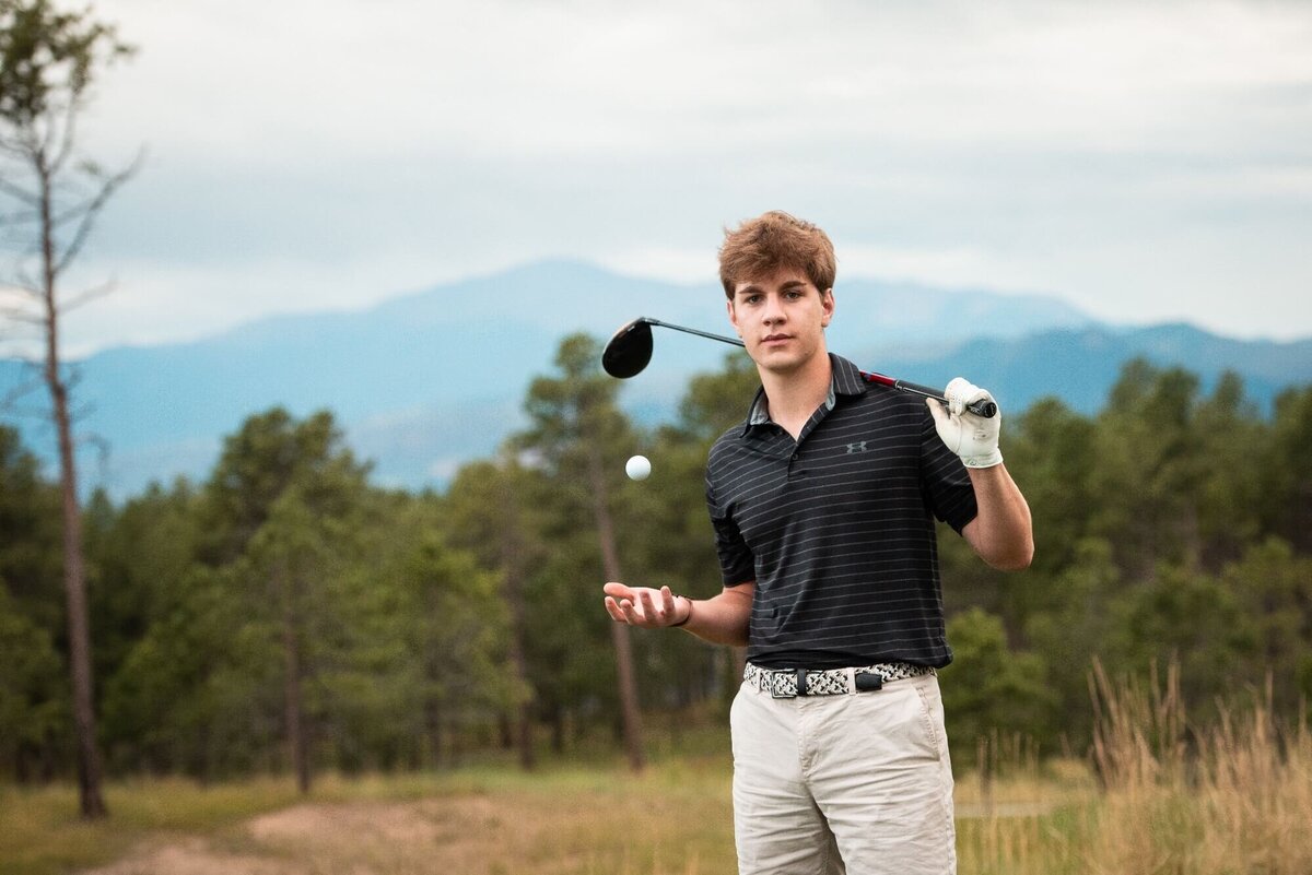 A high school senior in a black shirt tosses a golf ball while holding a driver over his shoulder