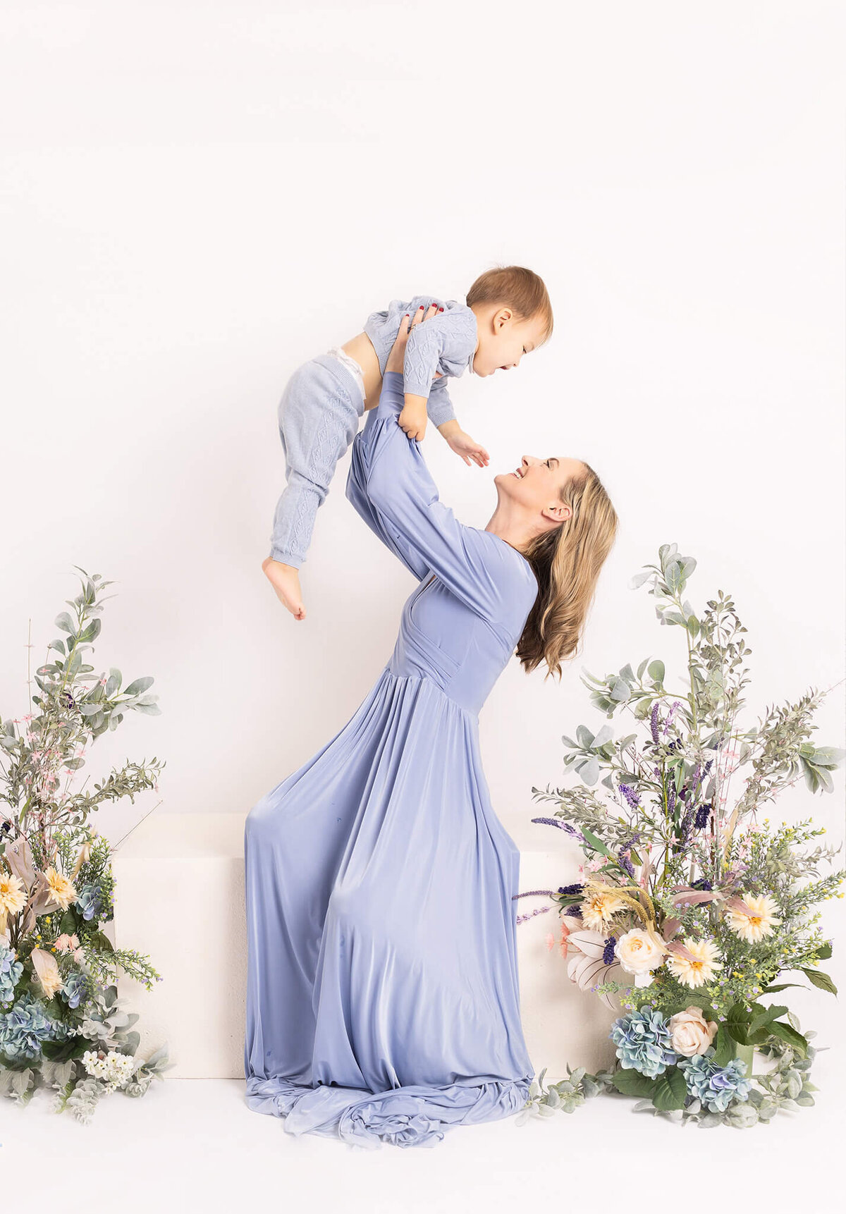 Mother lifting her son in the air laughing, both wearing blue