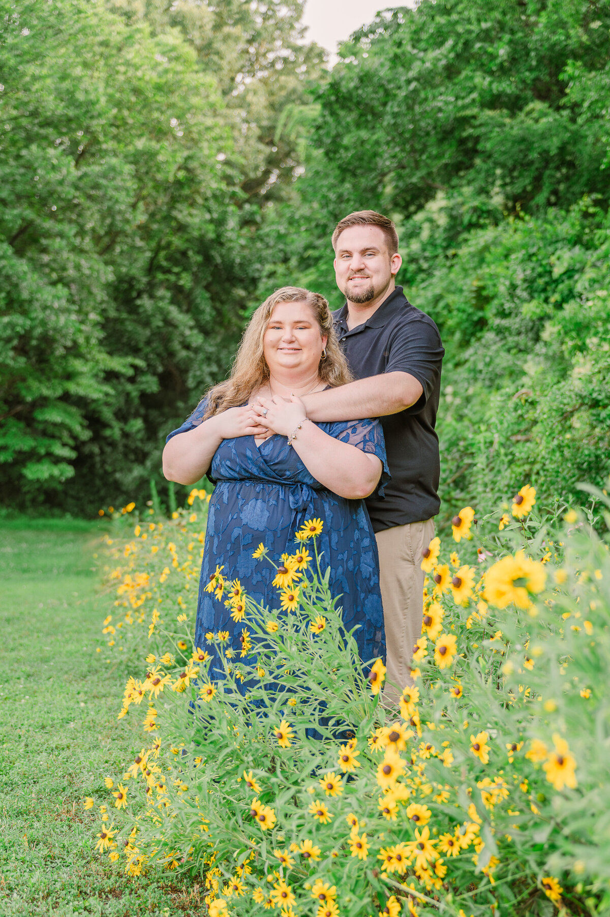 A happy engaged couple in a field of bright yellow sunflowers in Raleigh at sunset enjoying their destination wedding photography session with JoLynn Photography