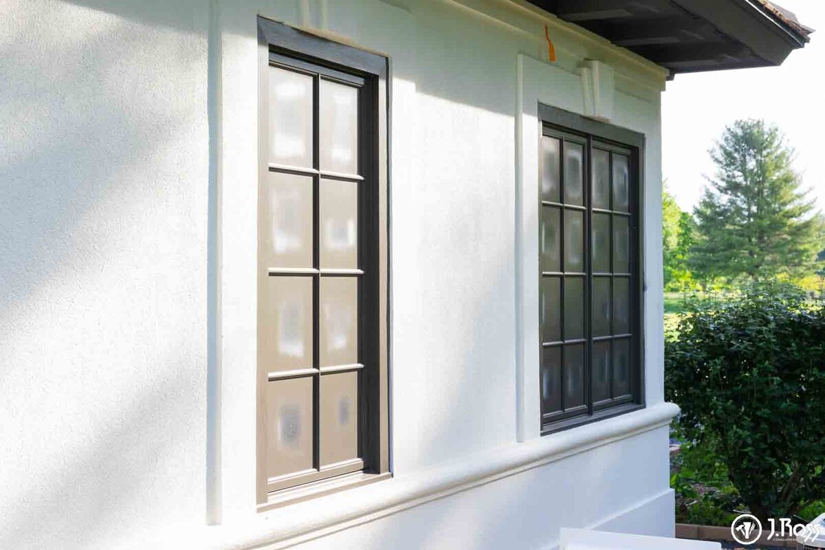 Close-up of newly finished dark-framed windows set into the bright white textured stucco wall, illustrating the clean lines achieved with professional home exterior painting Bristol, VA.