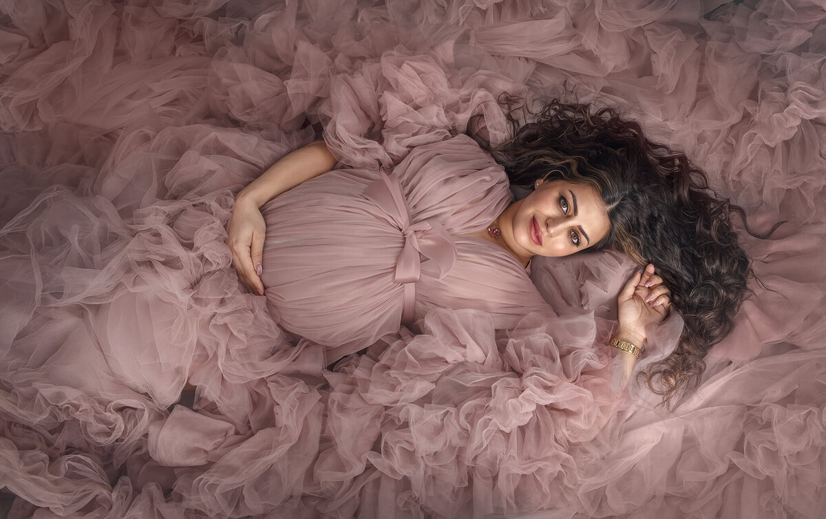 "Expecting mom in a pink ruffle gown, looking up, during a studio maternity photography session in Ottawa"
