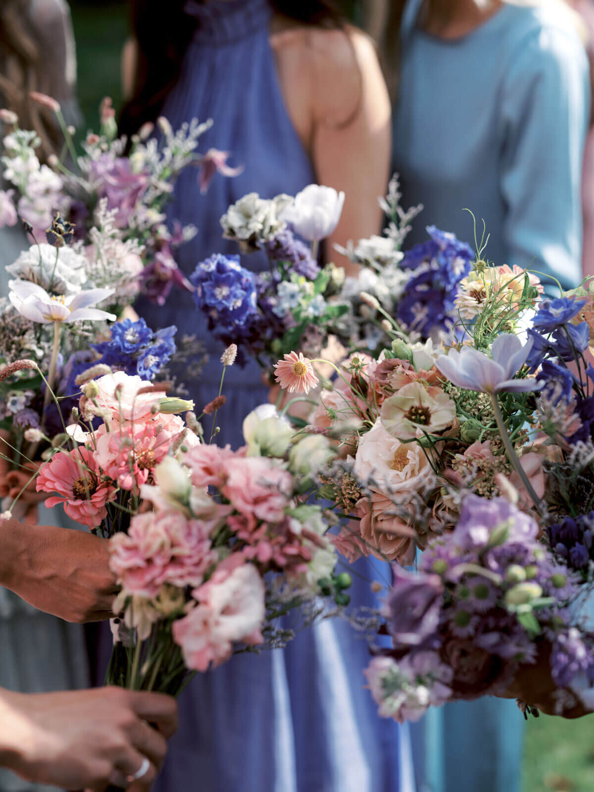 Close-up shot of blue, lavender, peach, and white flower bouquets, held by the bridesmaids at The Ausable Club, NY. Images by Jenny Fu Studio