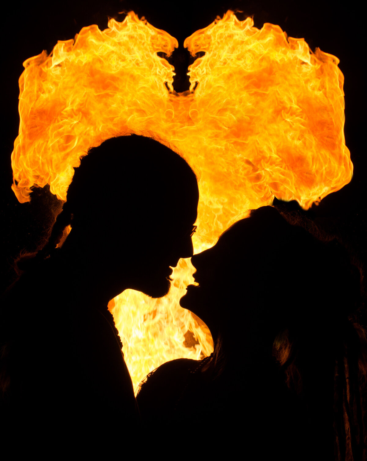 The silhouette of two people about to kiss with fire burning in the background.