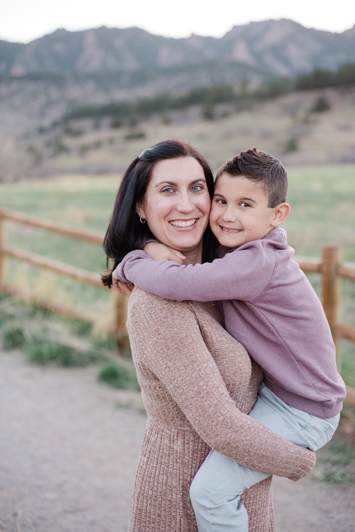 mom holds her young son and have their faces close together as they smile at denver family photographer with the boulder flat irons in the background