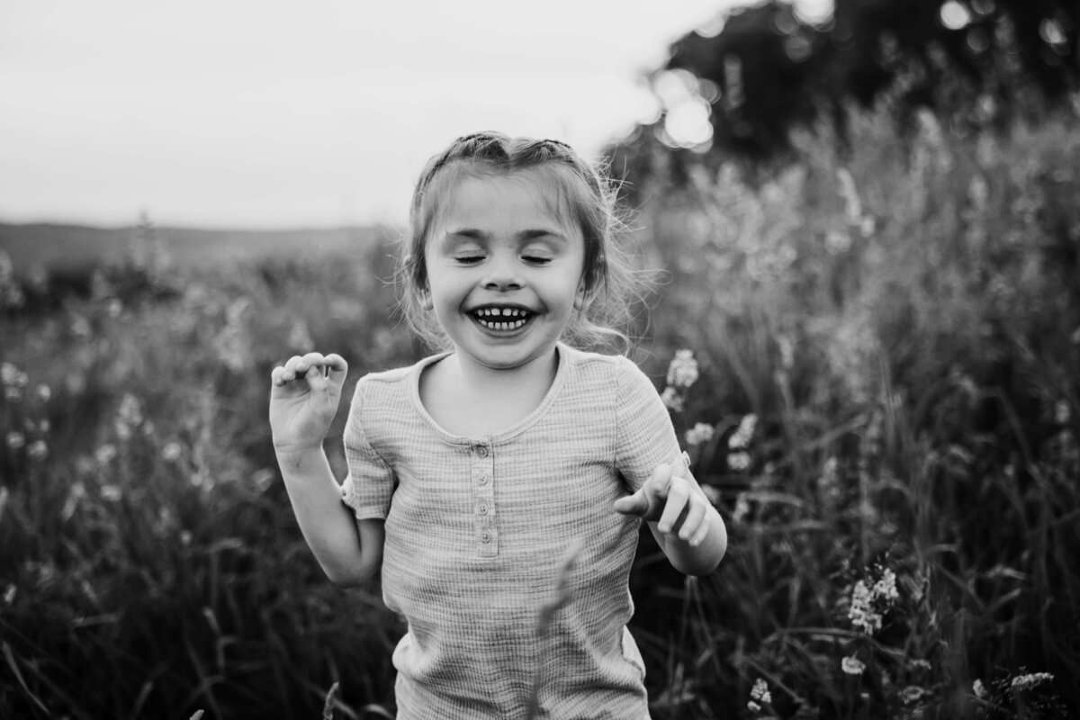 little girl in tall grass laughing in portrait session with reva davis photography