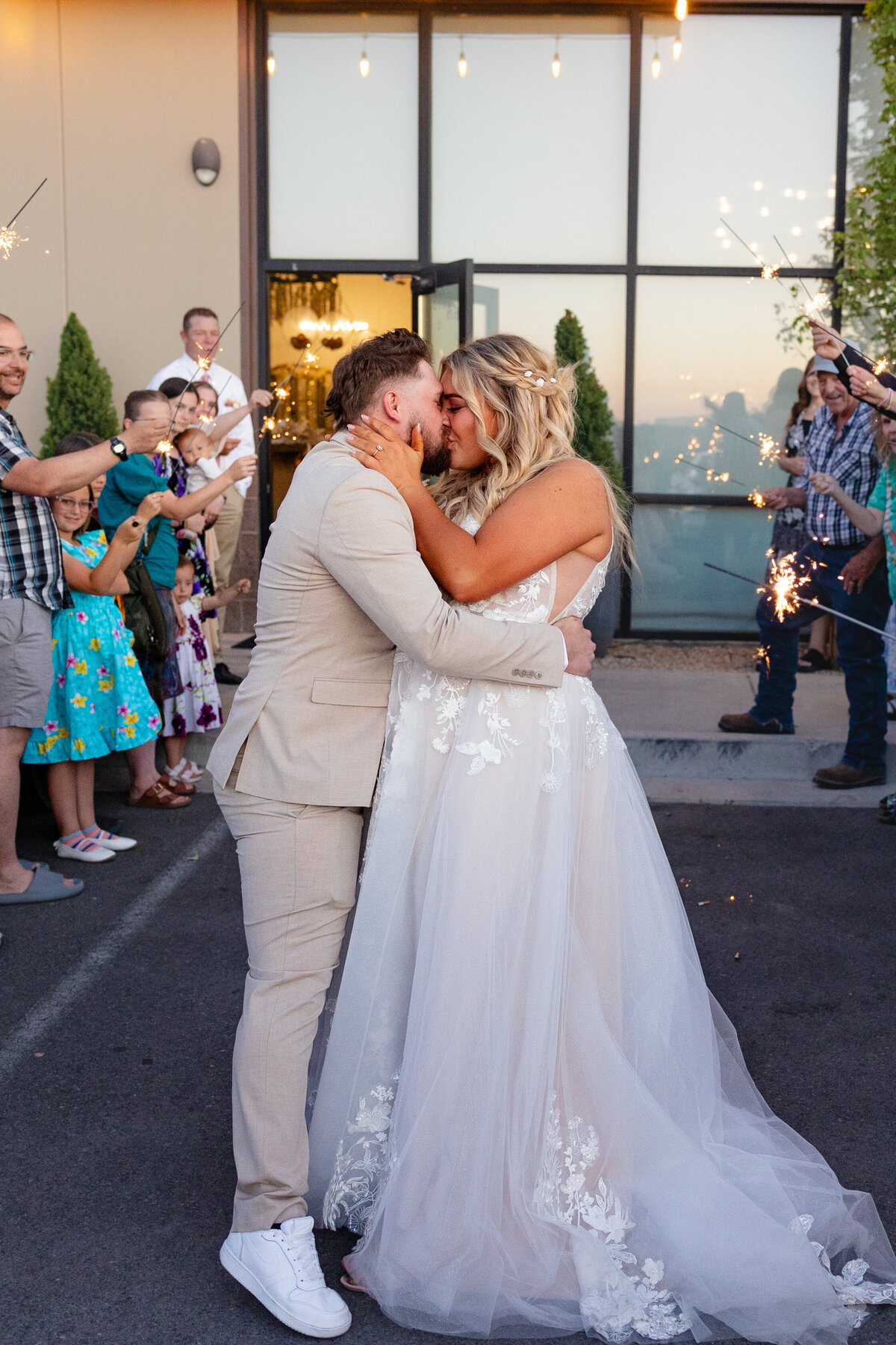 The bride and groom share a passionate kiss as they exit their wedding reception, surrounded by guests holding sparklers.