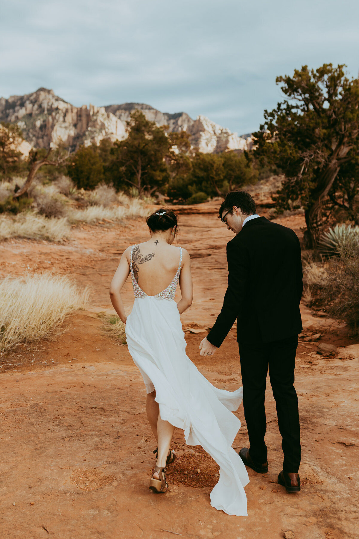 couple holding hands walks wiithin sedona landscape