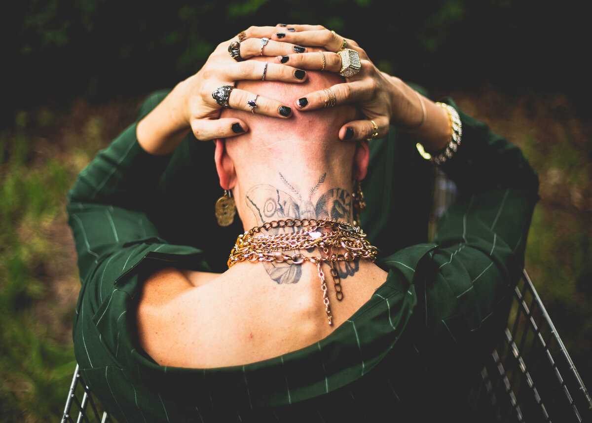 Man holding his head in his hands wearing lots of jewelry and a green suit and sitting in a shopping cart