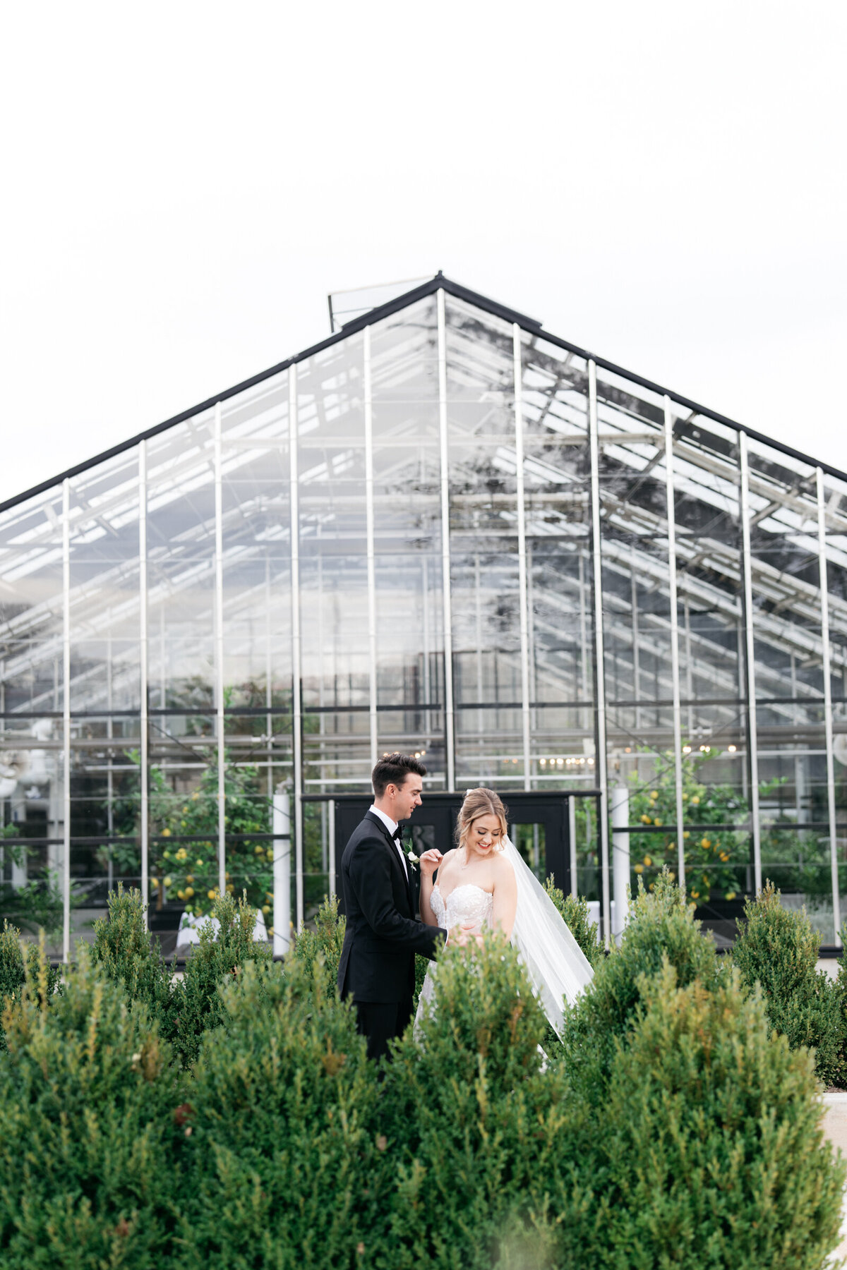 bride and groom posing together in front of a greenhouse