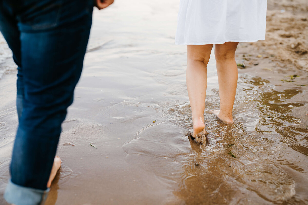 beach engagement photos of man and woman feet as they walk through the watery sand together