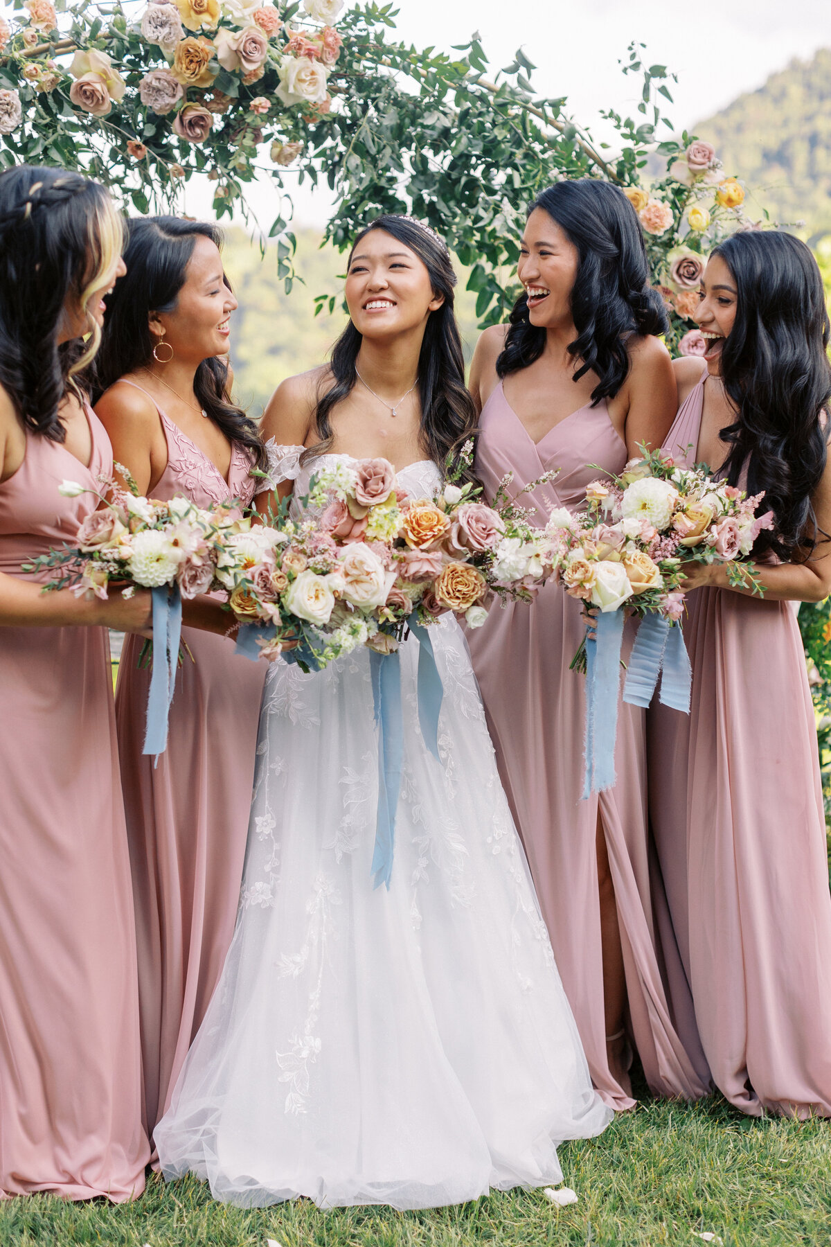 Bridesmaids holding bouquets in soft floral tones with blue ribbon accents at Castle Ladyhawke.