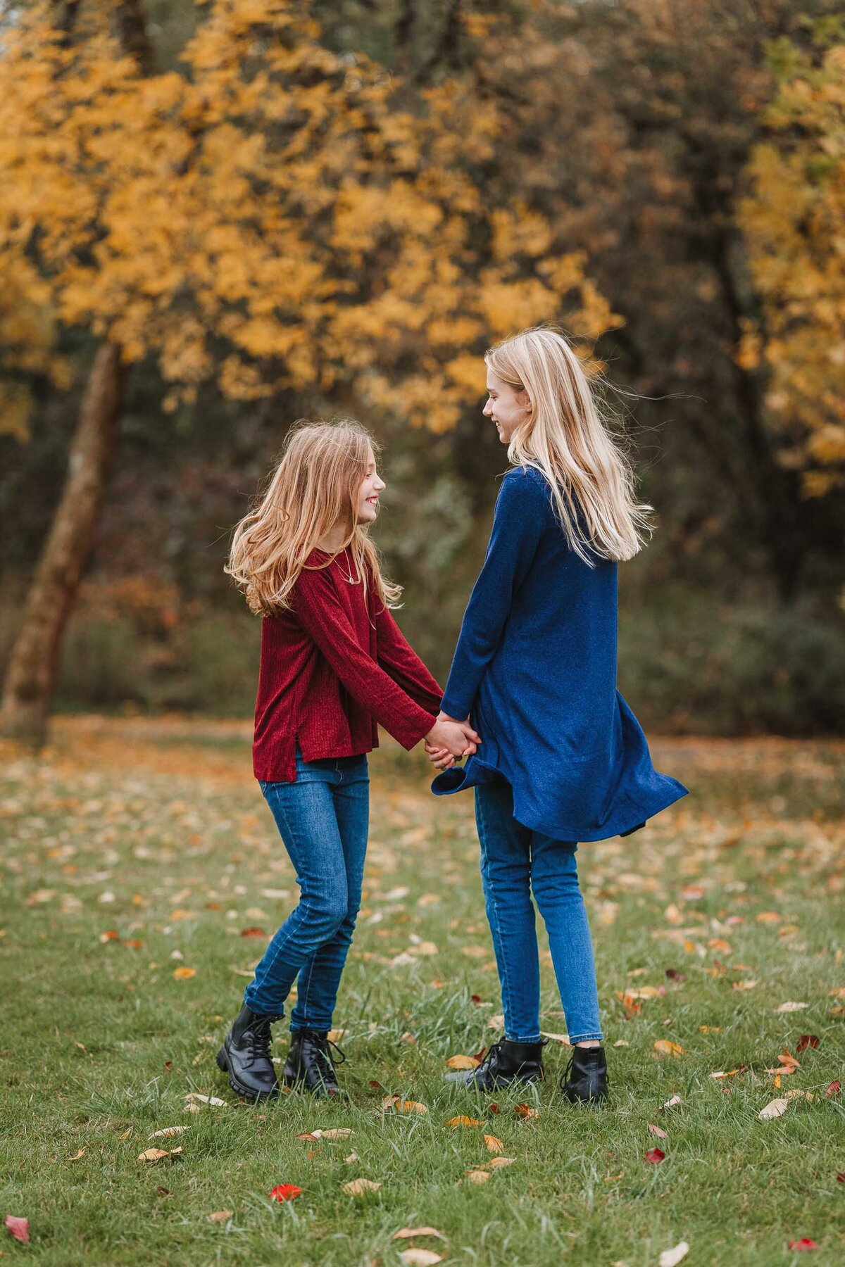 Two sisters joyfully dancing in a circle on Mercer Island, WA, surrounded by nature and sunlight during a fun family photo session.