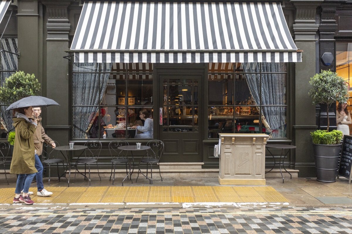 A couple walks past a Parisian cafe on a rainy morning in Paris, France. The Cafe is warm and Inviting.