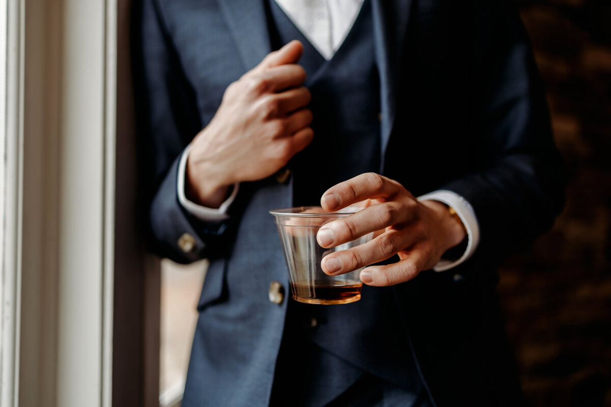 Groom holding a drink next to a bright window in a reception space at a Denver wedding venue boulder colorado