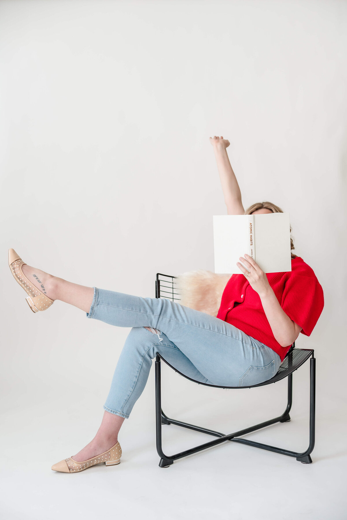 Playful female physician reading book with leg outstretched and arm raised in bright studio.