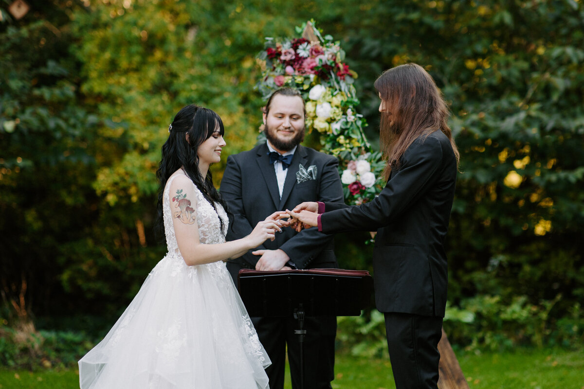 wedding couple exchanging rings with an officiant behind them