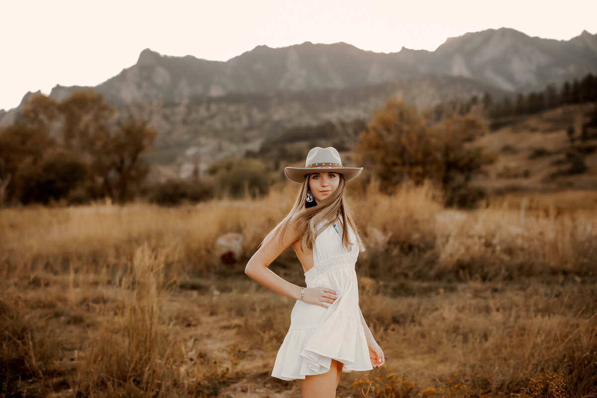 beautiful high school girl wearing a short white dress and a cowboy hat while hair is blowing in front of her face