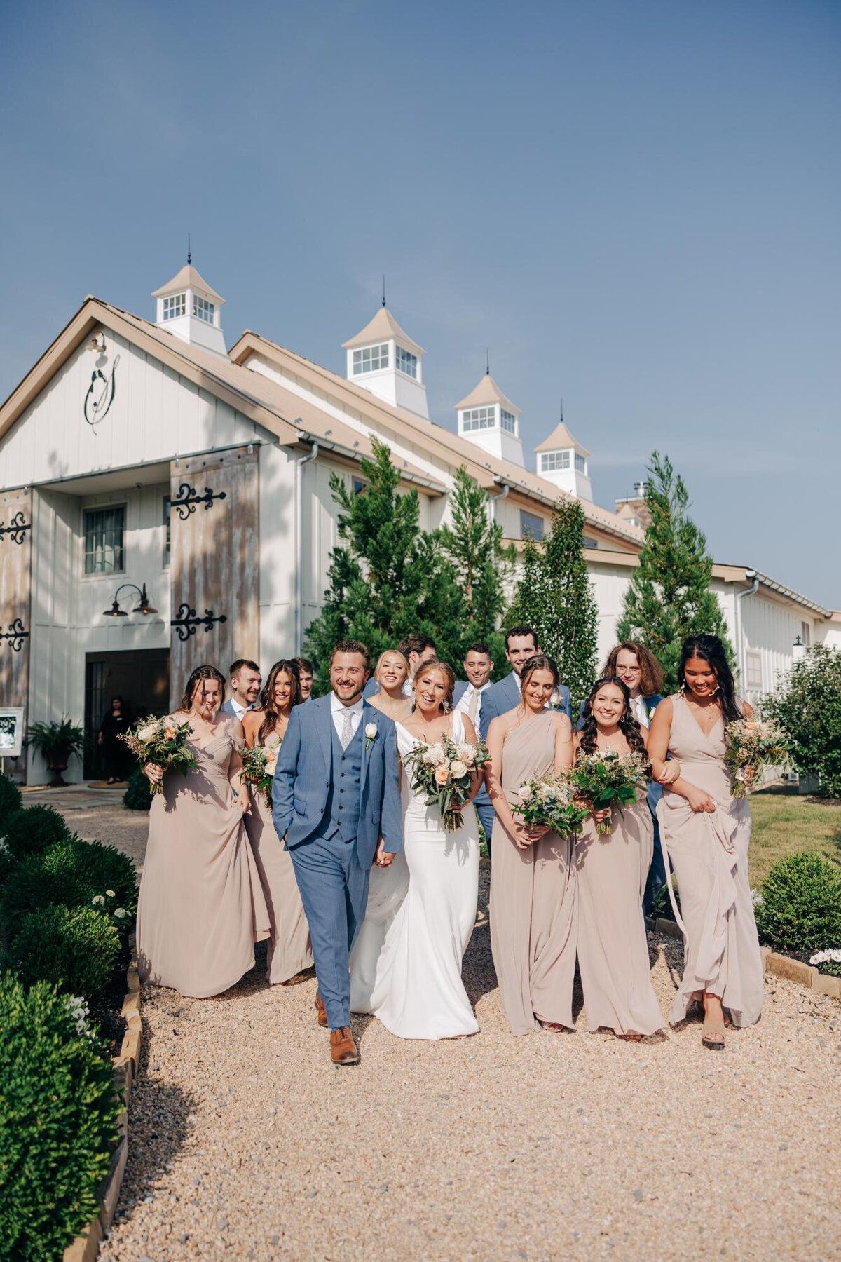 A wedding party posing outside a venue, with the bride and groom leading the group followed by bridesmaids and groomsmen.